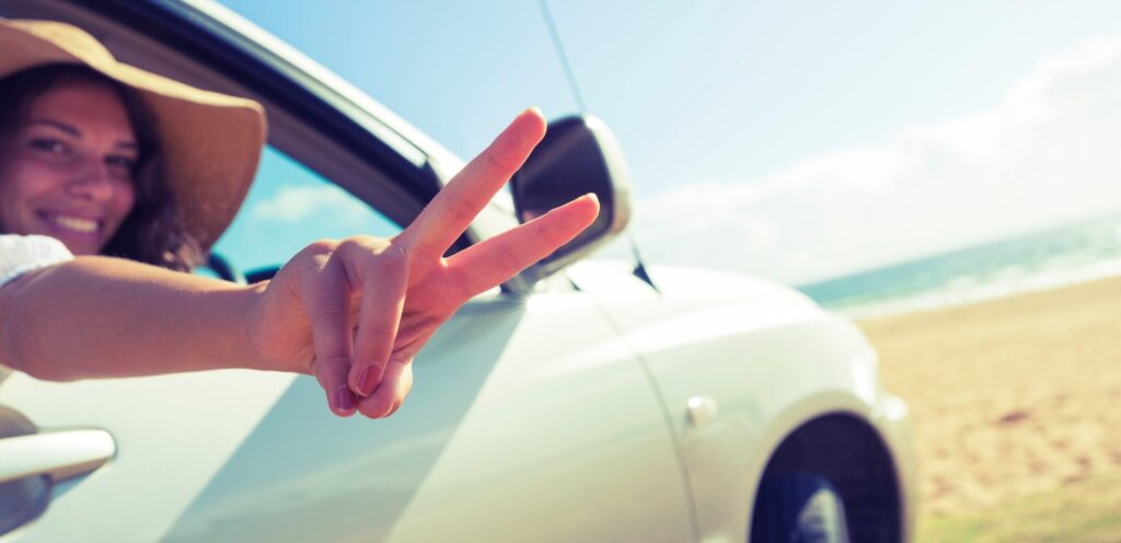 A woman throwing a peace sign from inside of a white vehicle