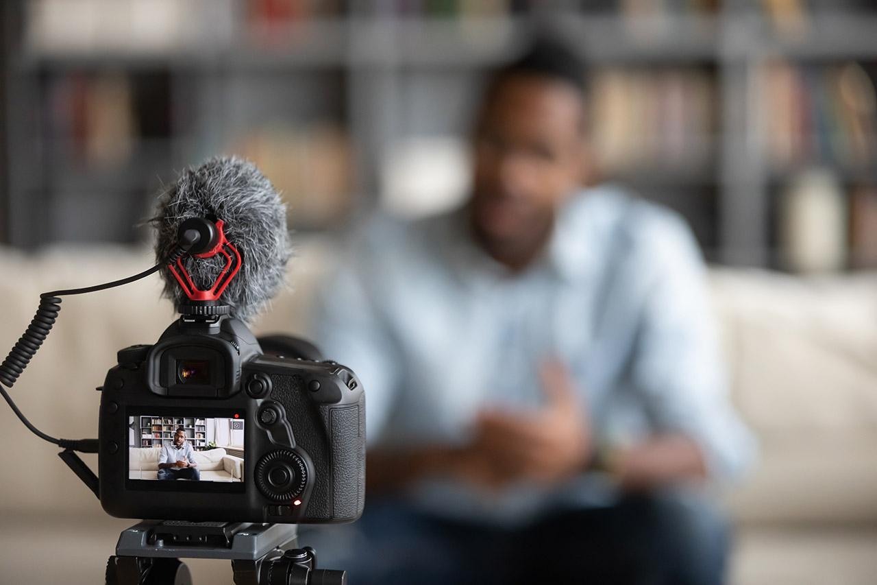 Close-up focus on a modern professional camera shooting a male instructor making course videos in the background.