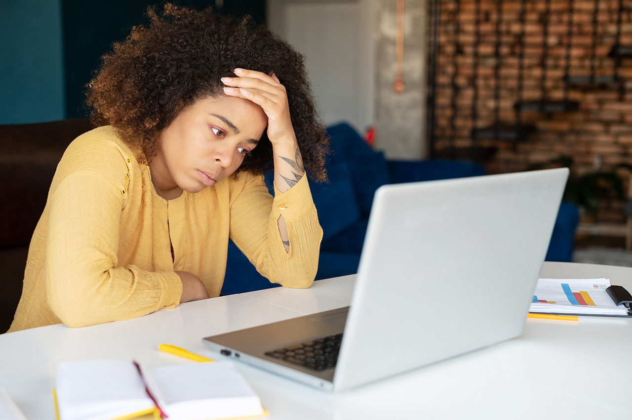 Weary woman feels stress, holds forehead and looks at the laptop screen with despair