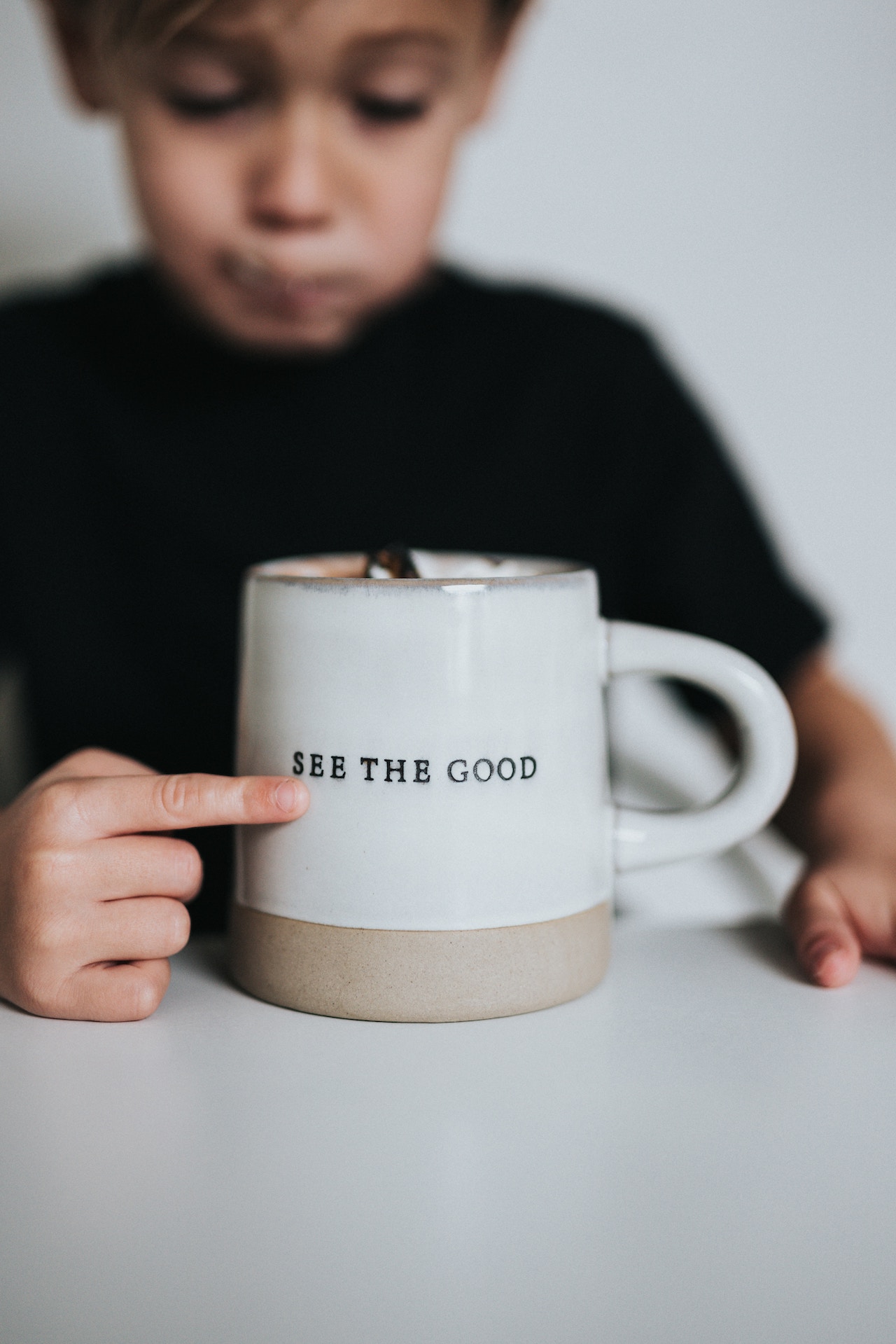 Child pointing at coffee mug that has text "See the Good"