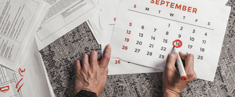 A person's hands writing on a calendar for September with a red marker.