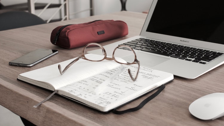 Glasses on a notebook, sitting in front of a laptop.