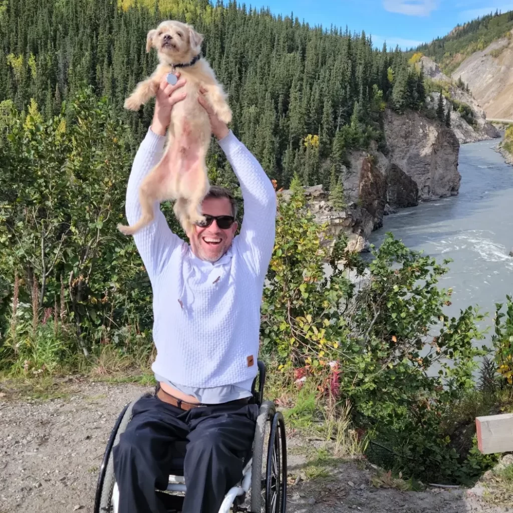 Brant holding his dog outside in Healy, AK with a river behind him