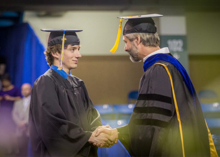 A graduate shaking the hand of faculty at graduation