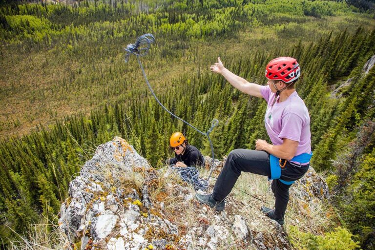 Climbers at the top of an outcropping, overlooking a boreal forest.