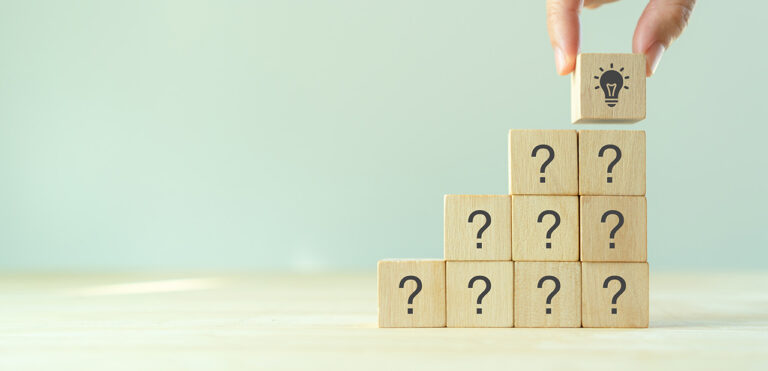 A series of wooden blocks with question marks on them that are stacked up 3 layers tall, with someone placing a single wooden block with a light bulb on the top.